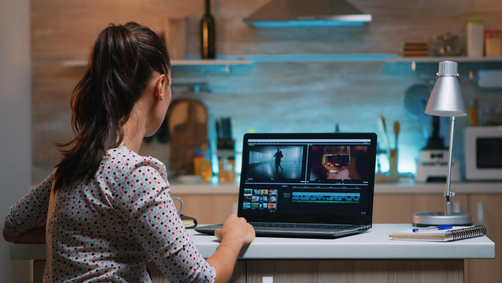 A woman with a ponytail is editing a video at the kitchen table